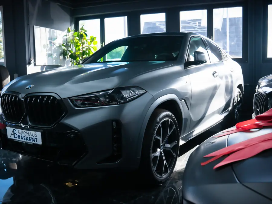 Grauer BMW X6 am Hallenfenster, daneben ein Fahrzeug unter roter Abdeckung